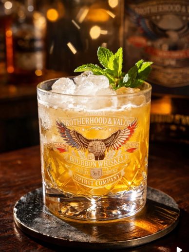 Bourbon whiskey cocktail with mint garnish in a branded glass on a tray.