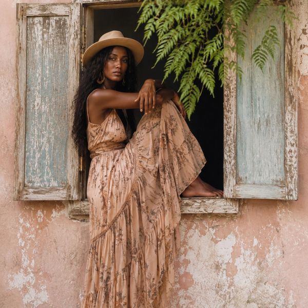 Woman in a flowing dress and hat posing in an old window frame.