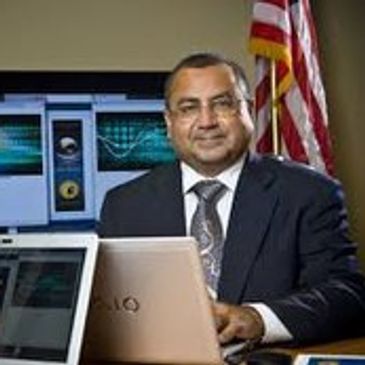 Man in suit sitting at a desk with laptop and American flag.