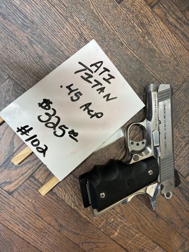 A silver ATI Titan .45 ACP handgun on a wooden floor with a price sign.