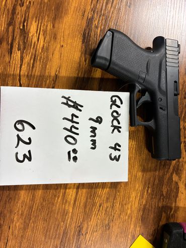 A Glock 43 9mm handgun on a wooden surface with a note showing price.