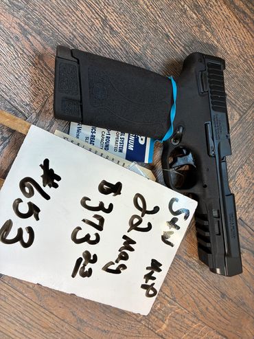 Black handgun with a note showing a phone number and text on a wooden surface.