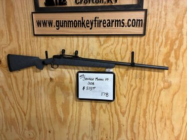 A Savage Model 10 .308 rifle displayed on a wooden wall with price and website.