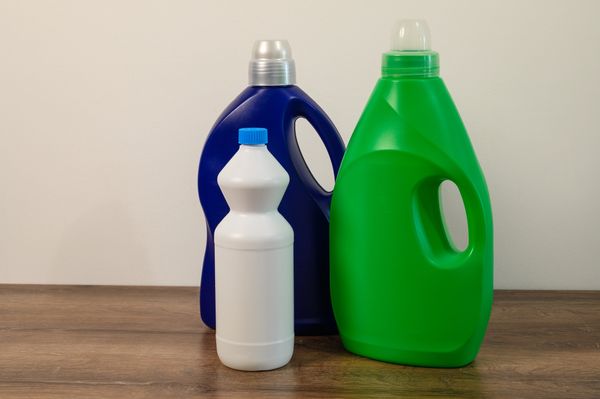 Three plastic bottles of cleaning supplies on a wooden surface.