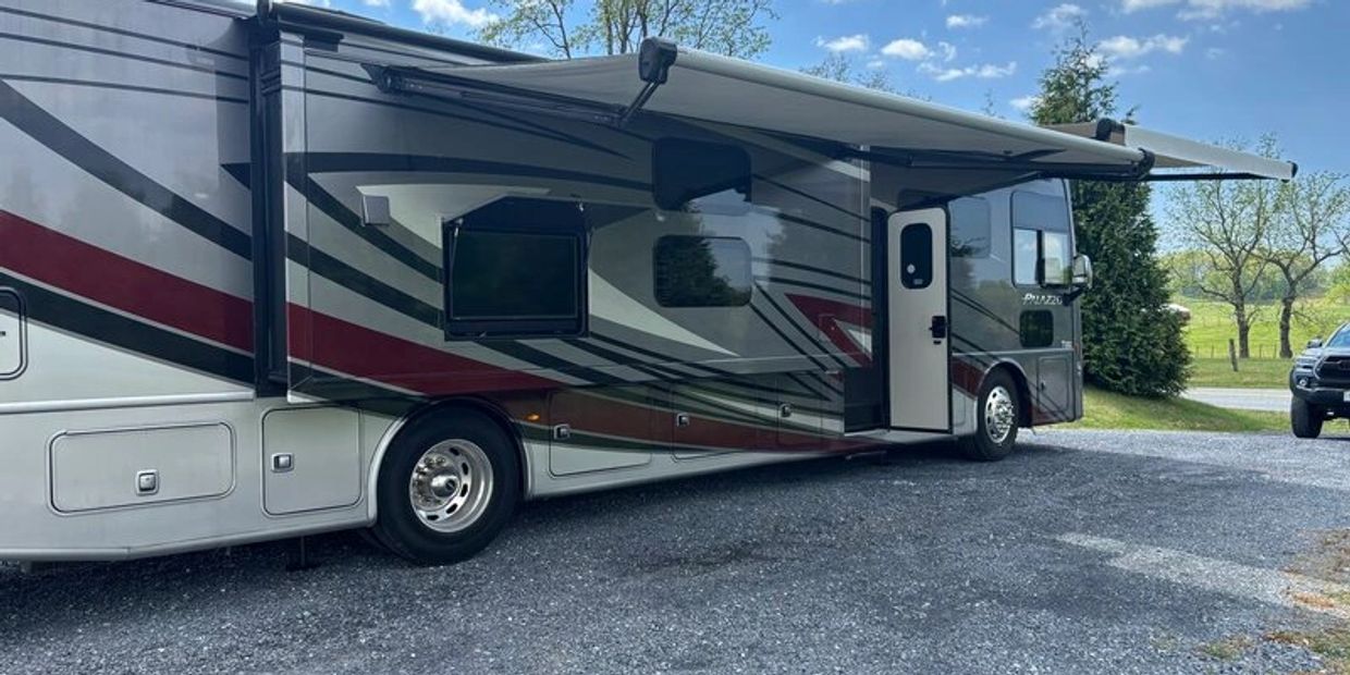 Parked motorhome with awnings extended on a gravel driveway.