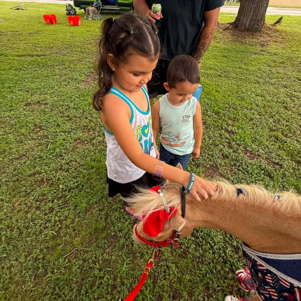 Two kids petting a small pony outdoors.