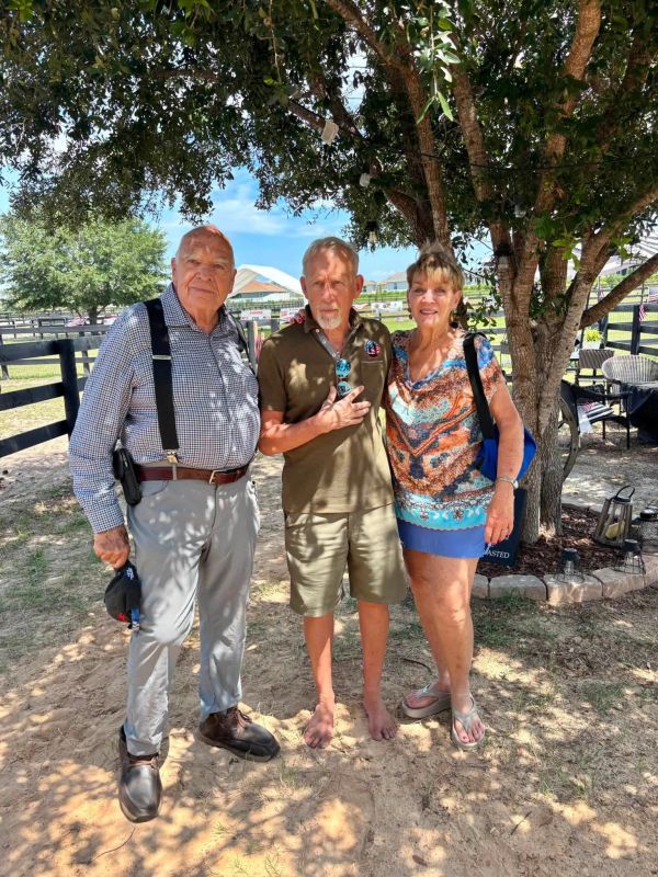 Three adults standing under a tree on a sunny day.