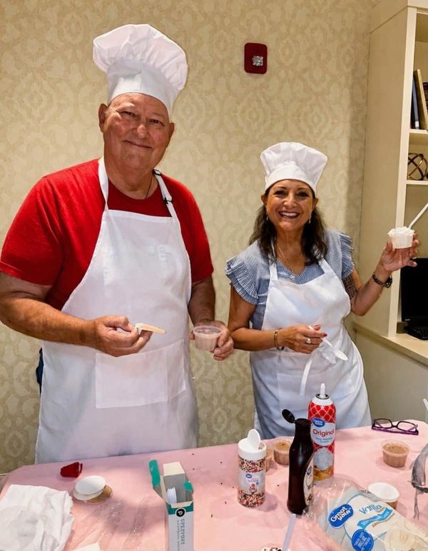 Two people in chef hats and aprons smiling with dessert items.