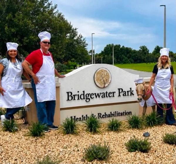 Three people and a pony in chef hats stand by a Bridgewater Park sign.