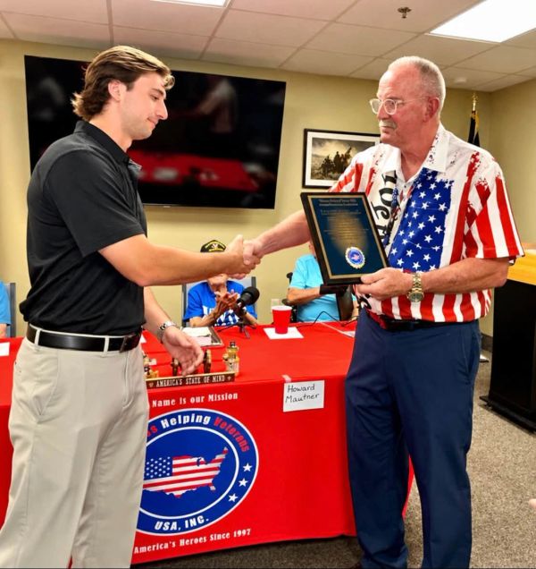 Man in patriotic shirt presents plaque, shaking hands.
