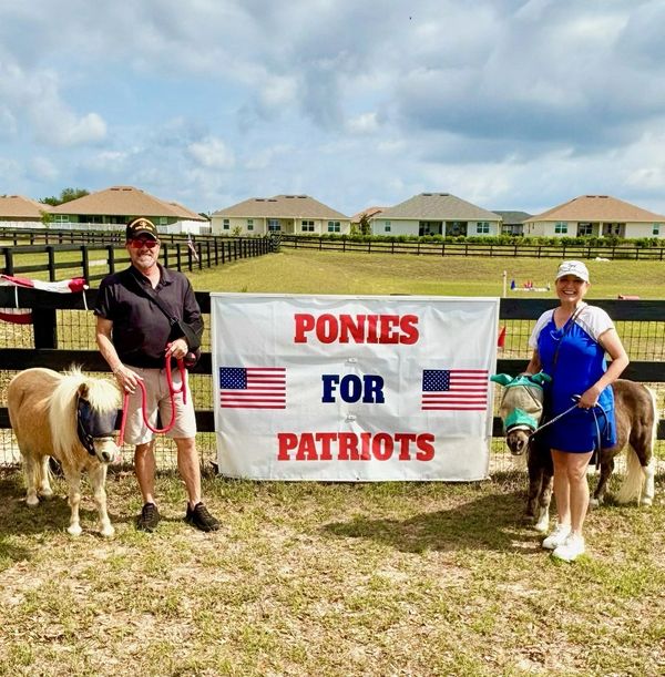 Two people holding ponies in front of a 'Ponies for Patriots' banner.