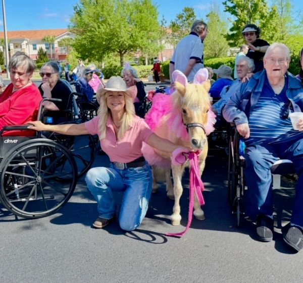 Woman with pony in pink tutu surrounded by elderly in wheelchairs.