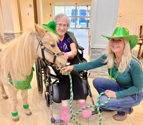 Elderly woman in wheelchair feeding pony with woman in green hat.