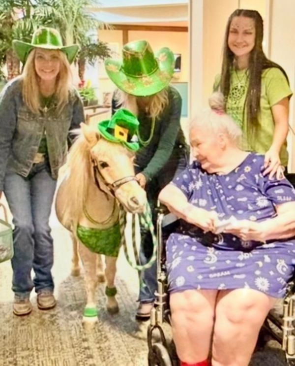 Older woman in wheelchair with three women and a pony wearing green hats.