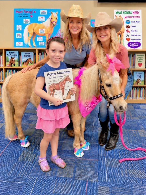 Young girl and two women with a pony in a library setting.