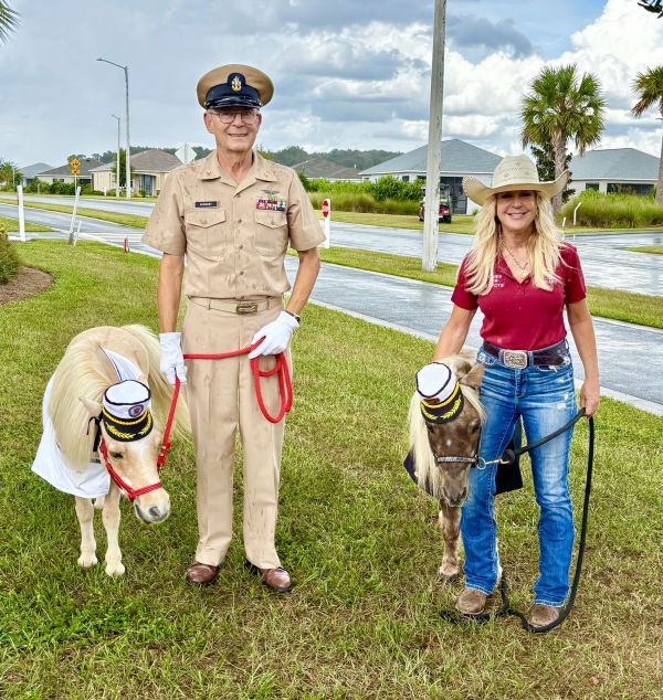 Man and woman with ponies dressed in hats on grass.