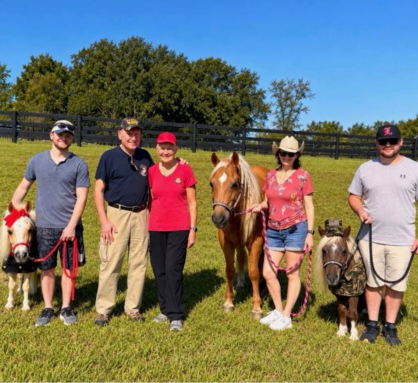 Group of five people with three small ponies in a field.