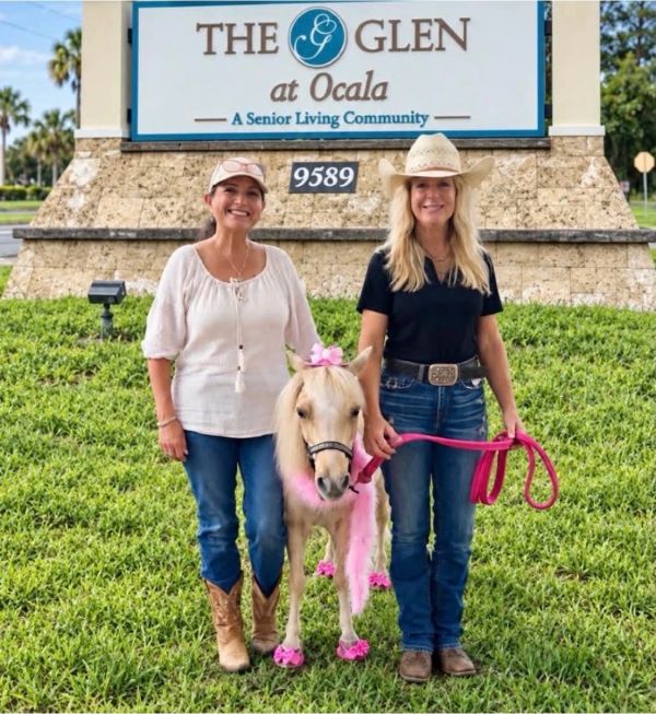 Two women with a decorated miniature horse at a senior living community.