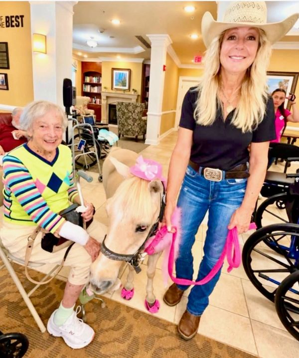 Elderly woman and caretaker with a small pony at a nursing home.
