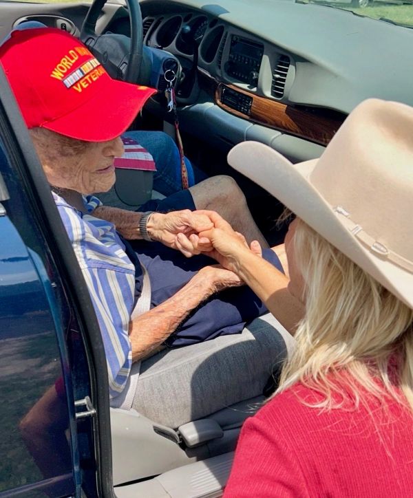 Older man in a car holding hands with a woman in a hat.