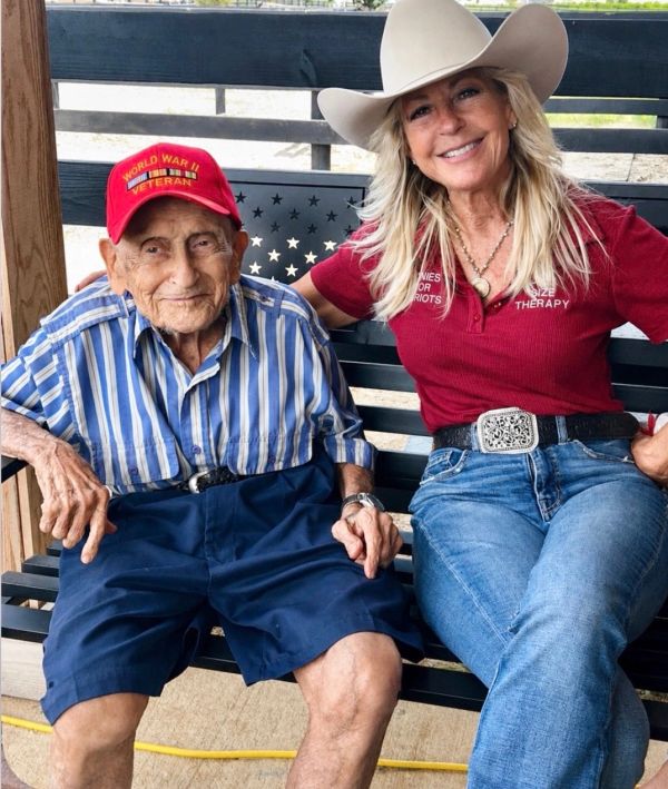 An elderly WWII veteran and a smiling woman in cowboy attire sitting together.