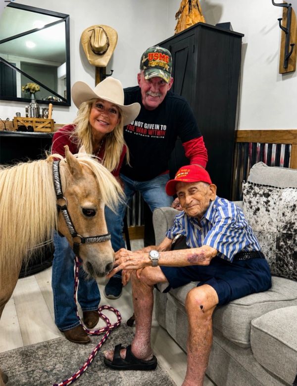 Three people and a small horse indoors, smiling and interacting.