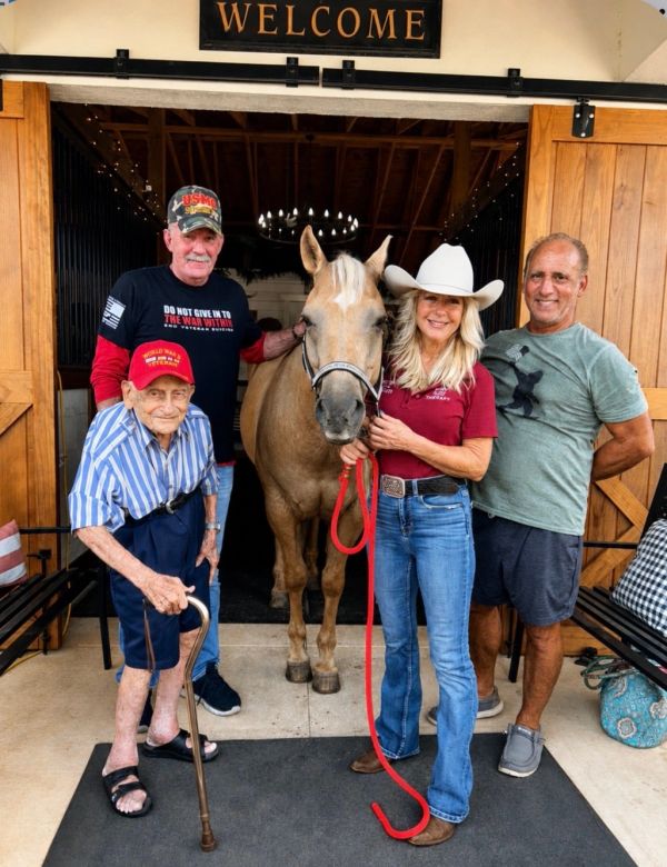 Group of four people posing with a horse under a welcome sign.