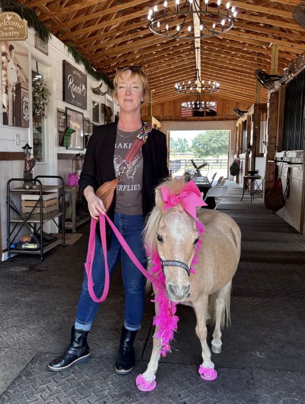 Woman standing with a decorated miniature horse in a barn.