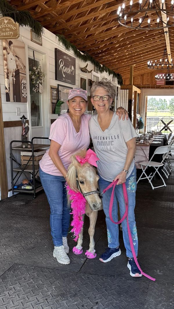 Two women posing with a decorated pony indoors.