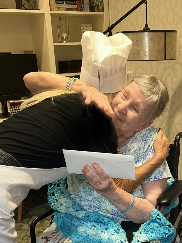 A warm hug between a chef and an elderly woman in a wheelchair.