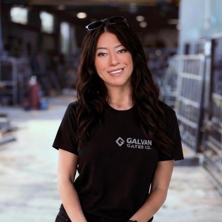 Owner of Galvan Gates Co. standing in the fabrication shop, wearing a branded black t-shirt, smiling