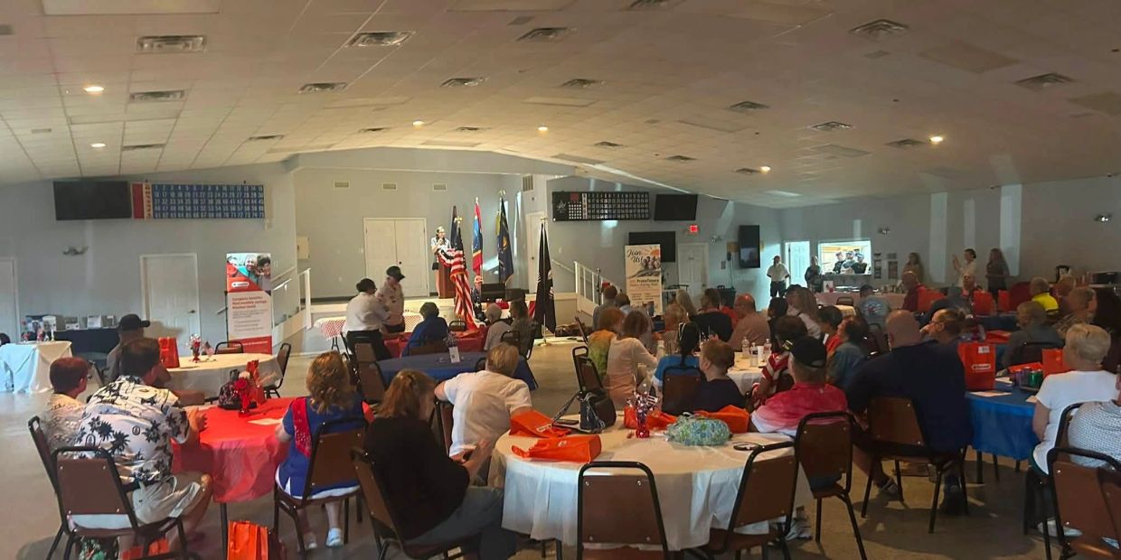 Community event with people seated at tables and a speaker on stage.