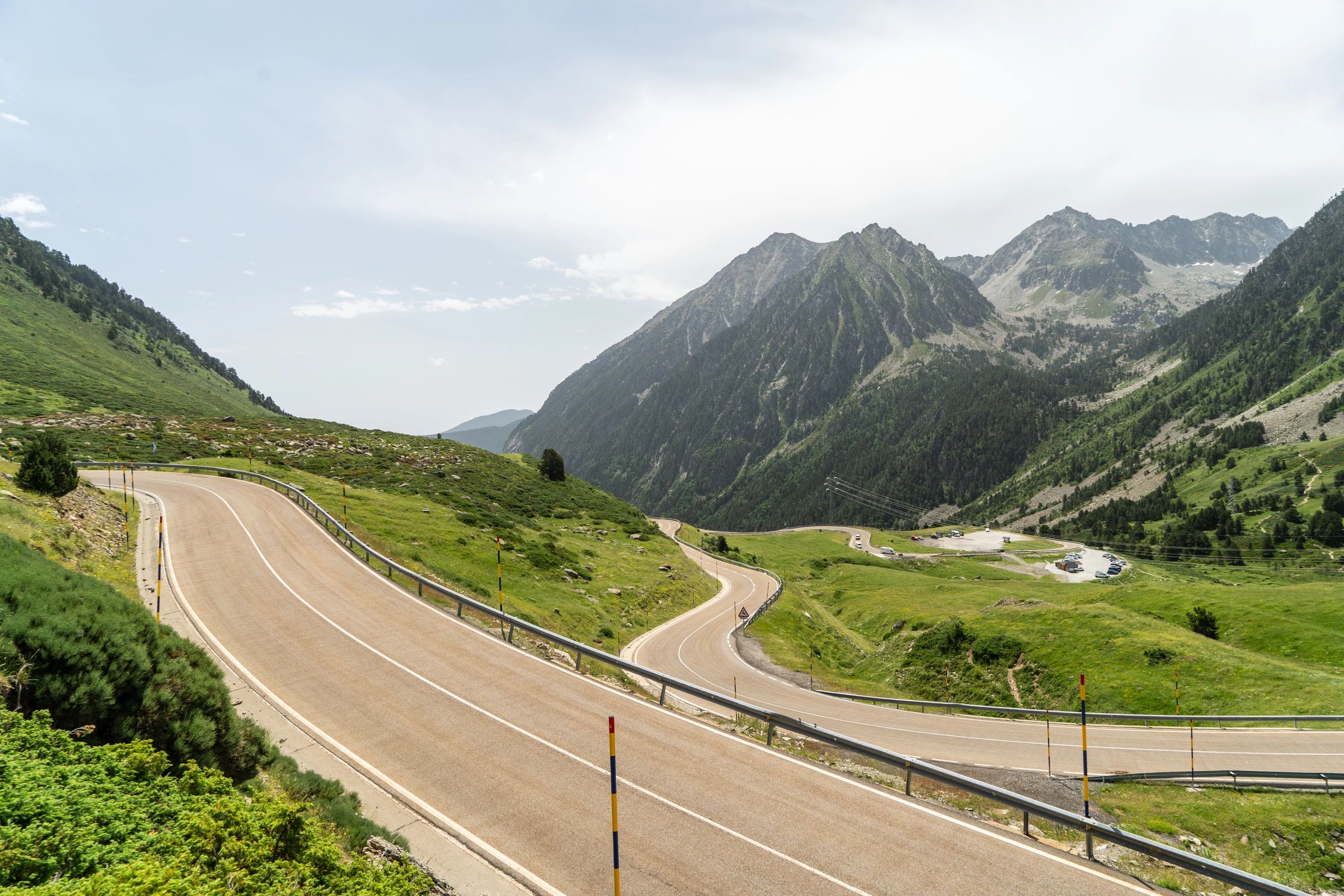 Winding mountain road with green hills and rocky peaks under a cloudy sky.