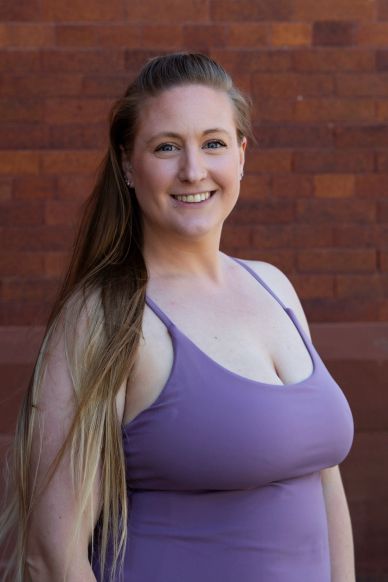 Smiling woman in a purple dress against a brick wall.