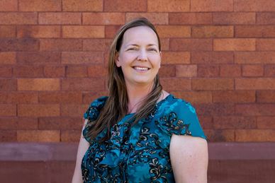 Smiling woman in teal blouse poses against brick wall.