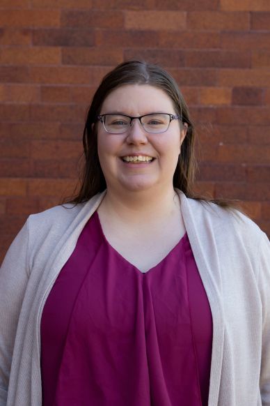 Woman smiling with glasses in front of a brick wall.