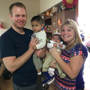 A happy couple holding two young children in a colorful room with toys.