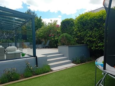 Modern backyard with patio, garden, and trampoline on artificial grass.