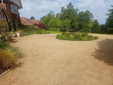 Gravel driveway with circular garden and lush greenery around a traditional house.