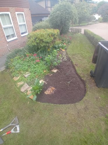 A freshly mulched flower bed with surrounding plants and garden tools nearby.