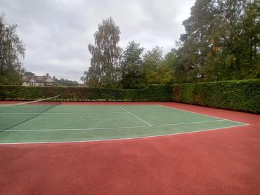 Empty tennis court surrounded by trees and a house in the background.