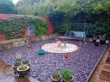 A tidy garden with slate chippings, potted plants, and a metal swing bench.