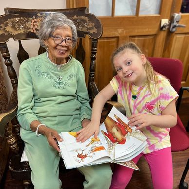 Senior and preschooler joyfully read together at  daycare in Tigard, OR.