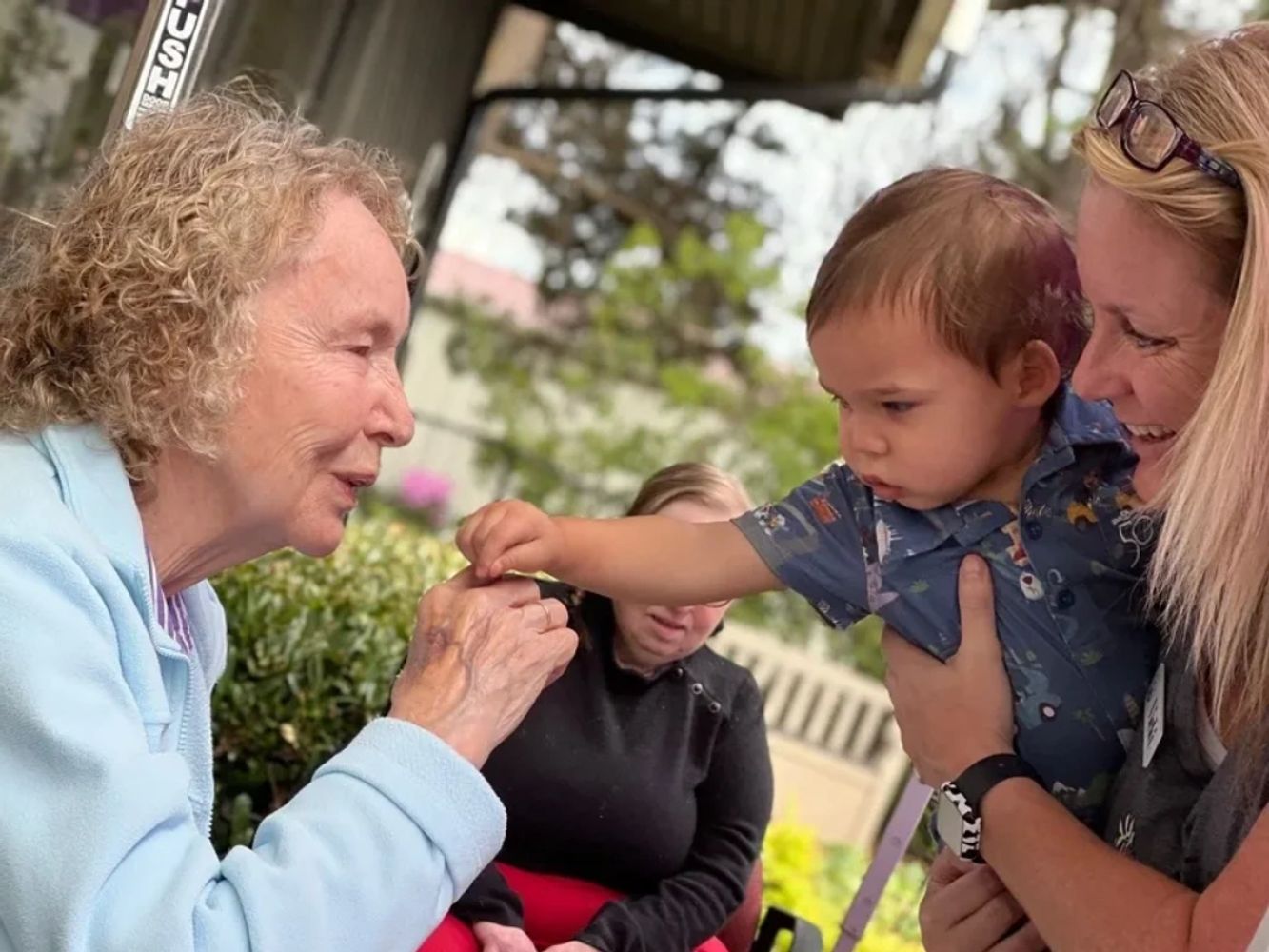 Senior smiles at child and caregiver at daycare in Tigard, OR.