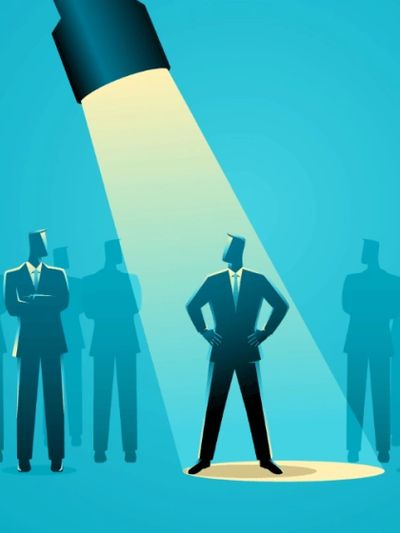 A spotlight highlights a confident businessman among others in shadow.