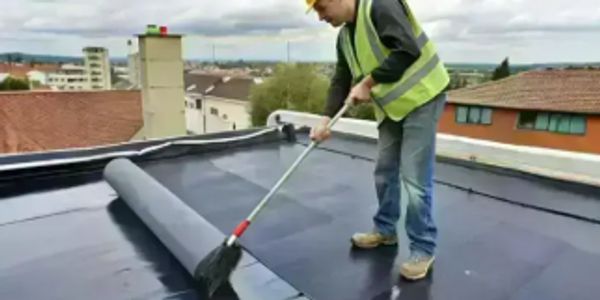 Worker installing waterproof membrane on flat roof.