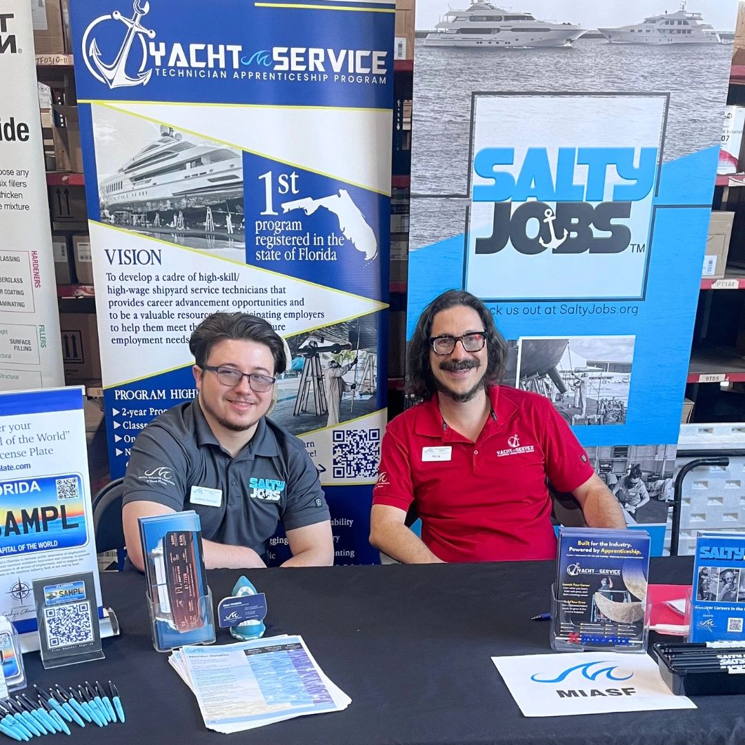 Two men at a Yacht Service apprenticeship booth promoting maritime careers.