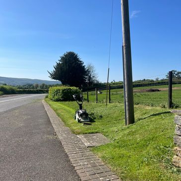 A lawn mower sits on freshly cut grass beside a rural road under a clear blue sky.