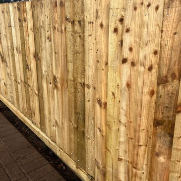 New wooden fence panels installed alongside a brick pathway.