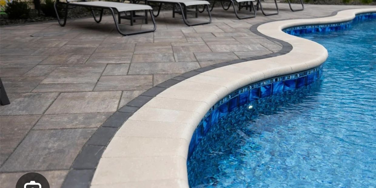 Curved pool edge with tiled border and stone patio.